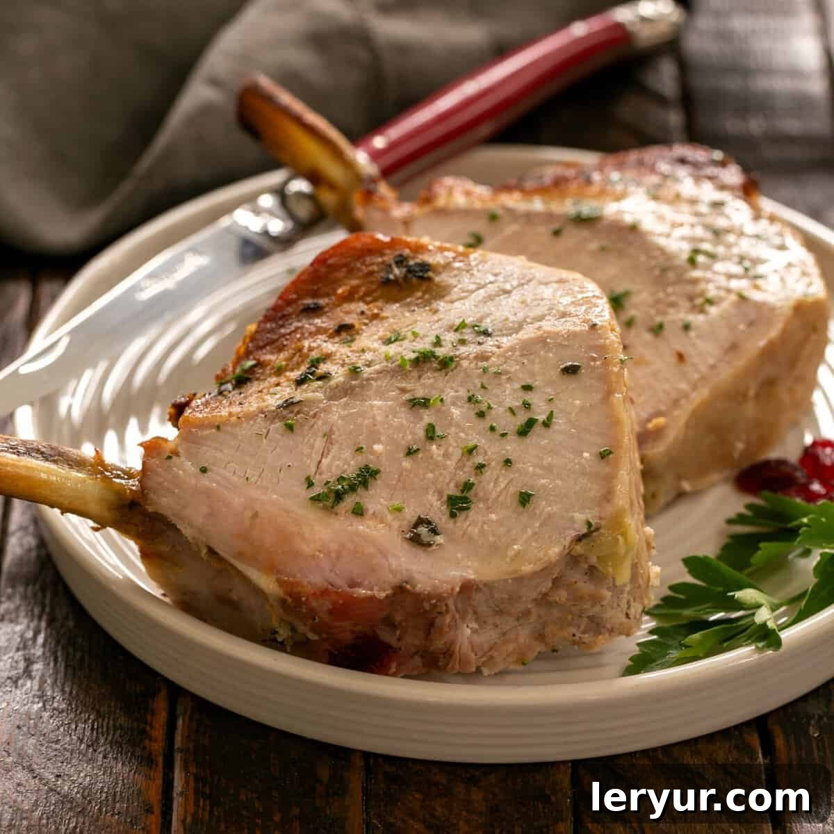 Regal Pork Crown with Spiced Apple Filling 2 Two exquisite slices of a perfectly cooked Crown Roast of Pork, elegantly presented on a pristine round white plate, ready to be served as a sophisticated entree.