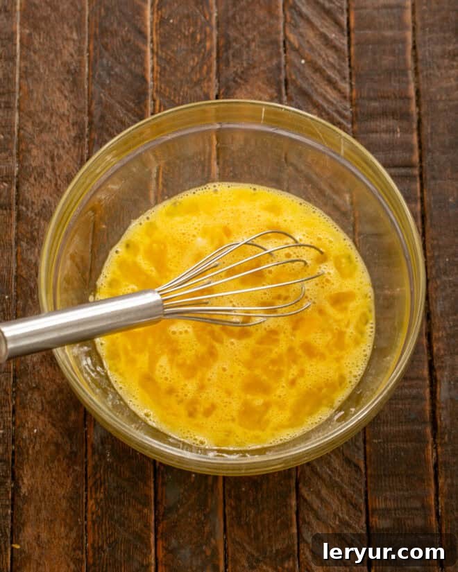 A bowl with eggs and sugar being whisked together, creating a pale yellow, frothy mixture.