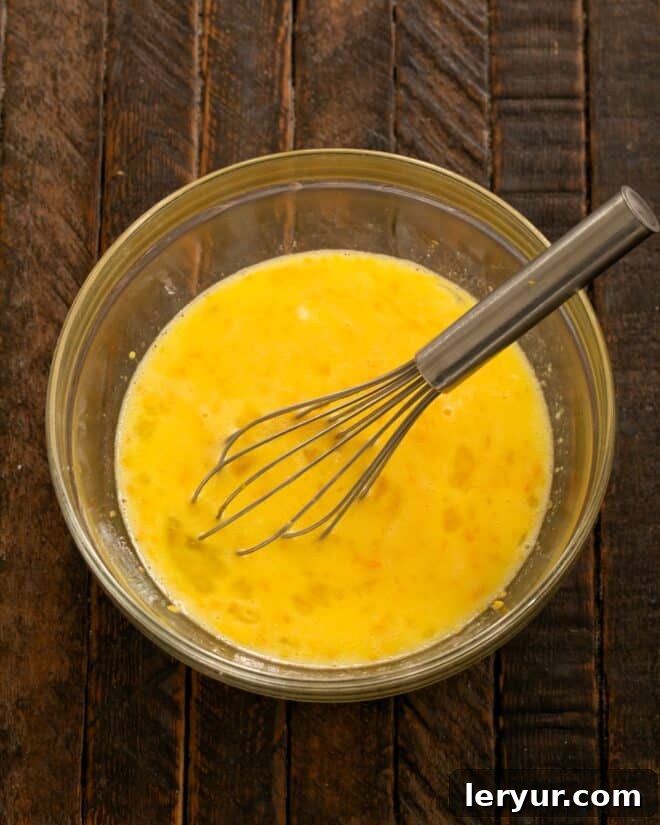 A close-up shot of lemon zest and freshly squeezed lemon juice being whisked into the creamy egg mixture.