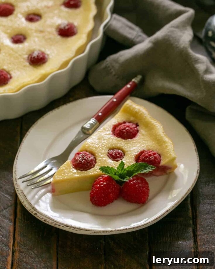 A beautifully presented slice of raspberry clafoutis on a white plate with a red handled fork, inviting you to taste.
