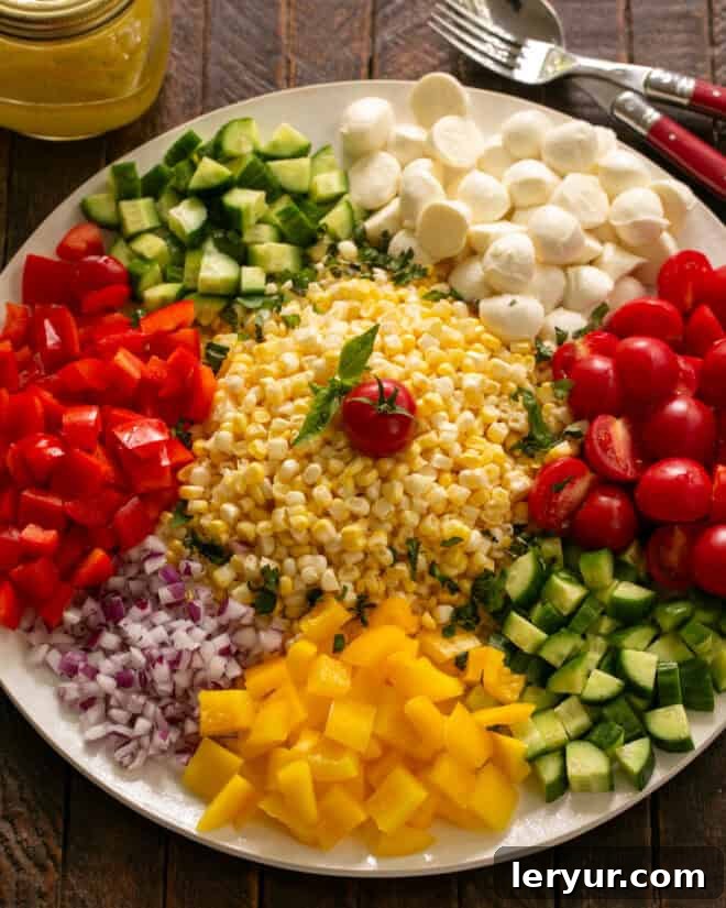 Kaleidoscope Summer Salad 5 Step 2: A large bowl filled with various chopped salad ingredients, including corn, tomatoes, bell peppers, cucumbers, and fresh mozzarella.
