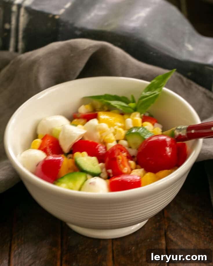 Serving of vibrant Chopped Summer Salad in a white bowl with a red handled fork, highlighting fresh ingredients.