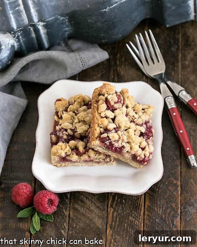 Two raspberry Crumble bars on a white dessert plate with 2 red handled forks.