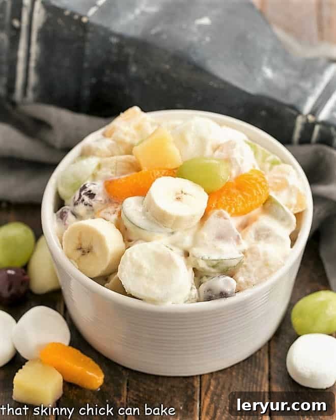 Holiday Fruit Salad with Marshmallows - A salad that's been in our family for 4 generations! A festive Holiday Fruit Salad with Marshmallows served in an elegant white ceramic bowl, surrounded by fresh fruits and extra marshmallows, ready for a holiday feast.