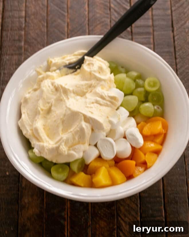 Holiday Ambrosia Salad 7 Pouring the creamy whipped cream and custard dressing over the fruit and marshmallows.