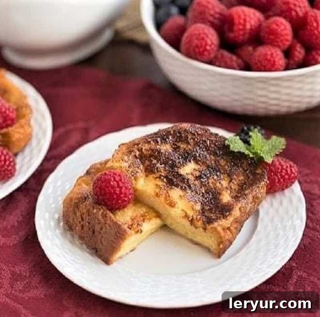 Sugar-Crusted French Toast Recipe - a double coating of sugar make this rich, eggy French toast dessert worthy! Sugar-Crusted French Toast Recipe cut in half and garnished with berries and mint on a white plate, showcasing the golden caramelized crust.