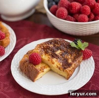 Sugar crusted French toast halves on a white plate with fresh berries and powdered sugar