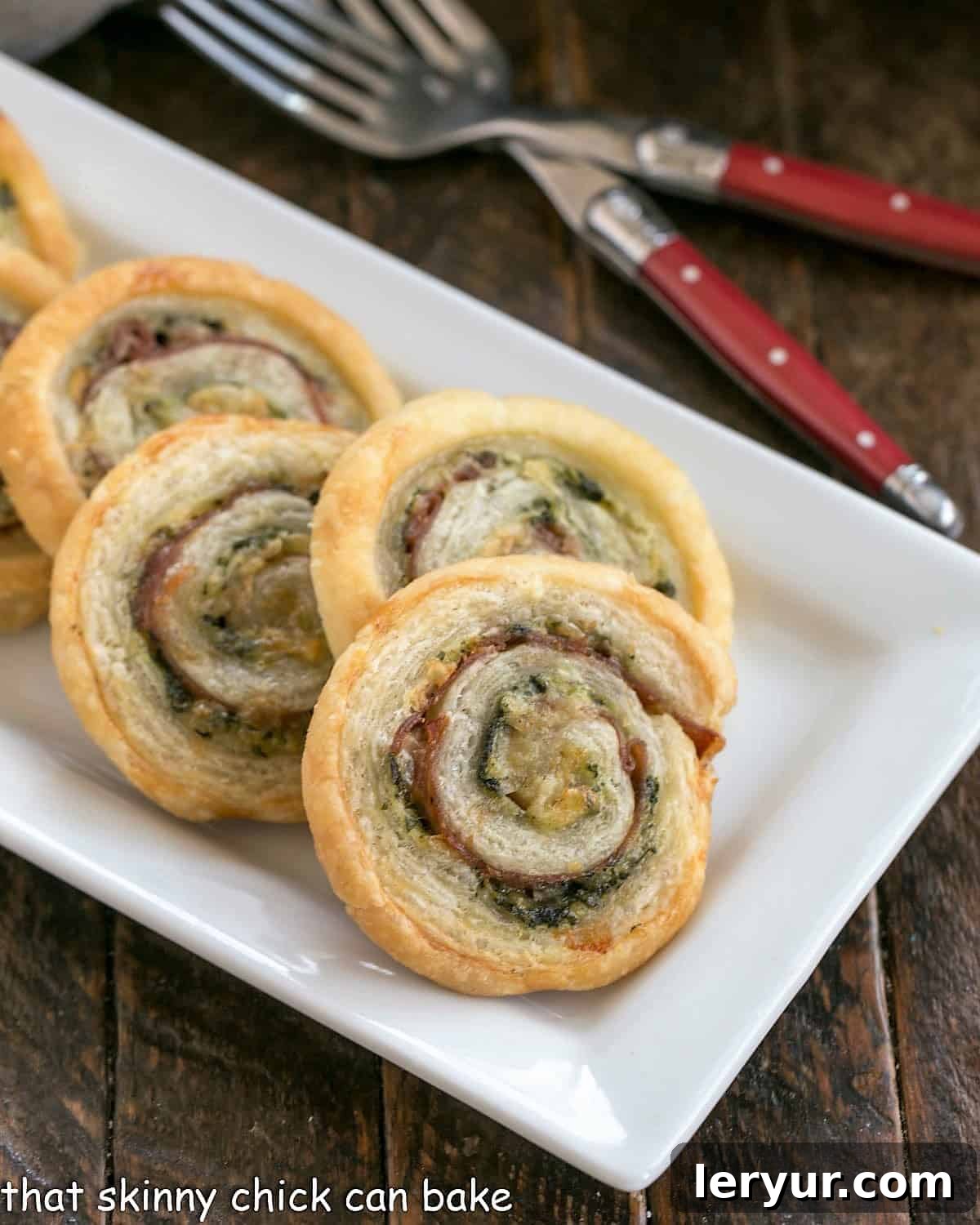 Prosciutto, Gruyere and Basil Pinwheels - an easy, elegant puff pastry appetizer that's a breeze to prepare Close view of Prosciutto, Gruyere and Basil Pinwheels on a white ceramic tray with 2 forks.