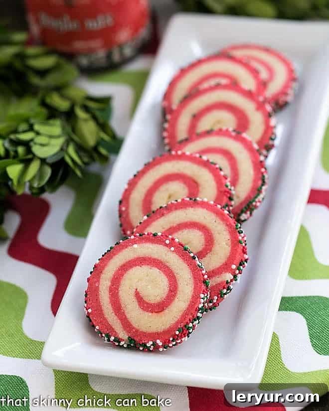 Holiday Pinwheel Cookies - Delicious, buttery and festive Christmas cookies that are adaptable to any holiday! Close-up of baked Holiday Pinwheel Cookies arranged neatly on a narrow white ceramic tray, highlighting their perfect spirals.