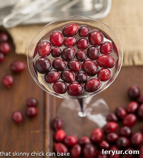 White Cosmopolitans in a martini glass topped with fresh cranberries.