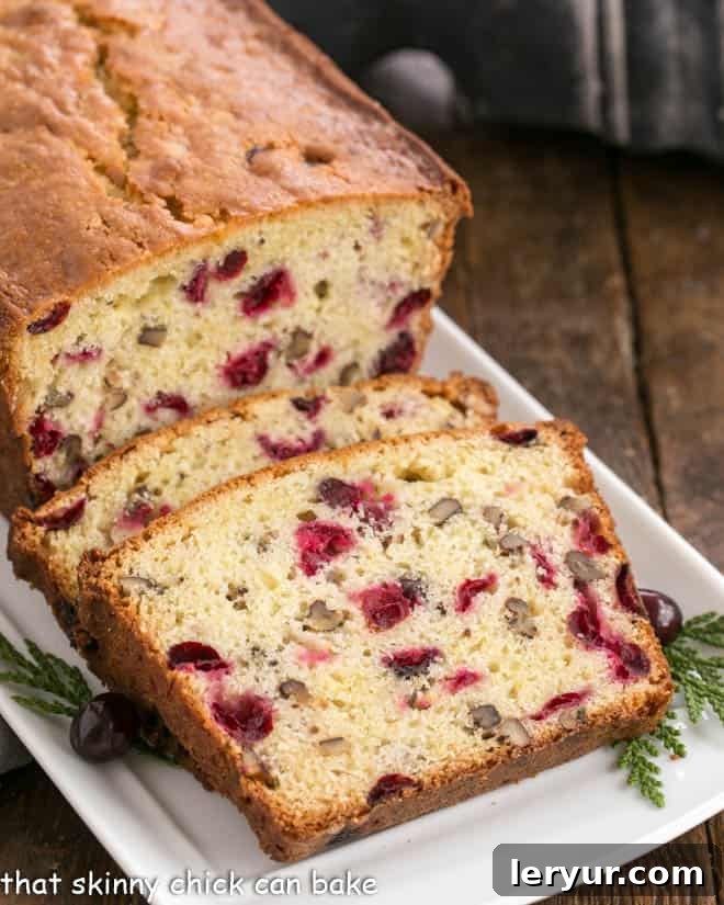 Classic Cranberry Pecan Bread is perfect for the holidays. The sweet-tart, crunchy-crispy components of this cranberry quick bread recipe make this a loaf to remember! Slices of cranberry pecan quick bread on a white tray, showcasing the vibrant red cranberries and golden pecans.