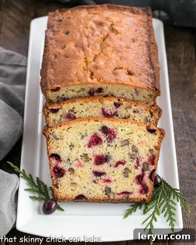 Classic Cranberry Pecan Bread is perfect for the holidays. The sweet-tart, crunchy-crispy components of this cranberry quick bread recipe make this a loaf to remember! A beautifully baked loaf of cranberry bread on a white tray, with two perfectly sliced pieces in front, ready to be enjoyed.