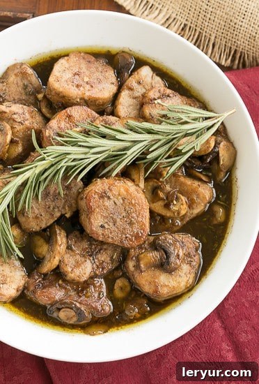 Pork Tenderloin Medallions in a white serving bowl topped with a sprig of rosemary.