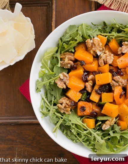 Overhead view of Arugula Salad with Roasted Butternut Squash in a white bowl, garnished with Parmesan shavings and offering a glimpse of the rich textures.