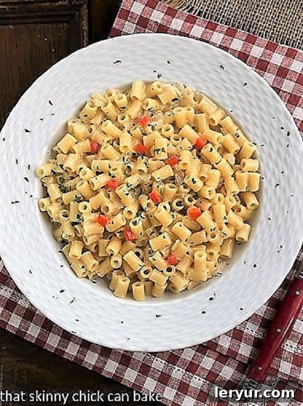 Overhead view of creamy pasta risotto in a white bowl, resting on a charming red and white checkered napkin. The dish is adorned with fresh herbs, showcasing its rich texture and appetizing appeal.