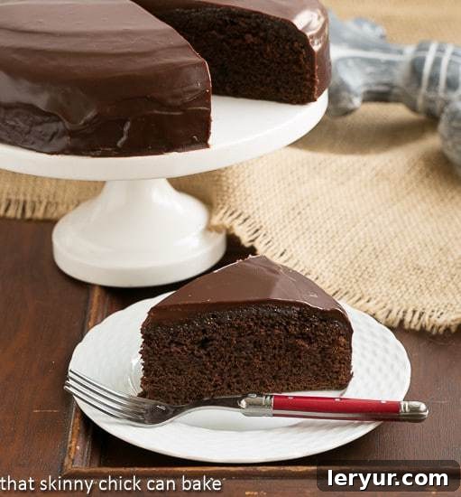 A rich One Layer Fudge Cake with a glistening chocolate ganache topping, served on an elegant white dessert plate, ready to be enjoyed.