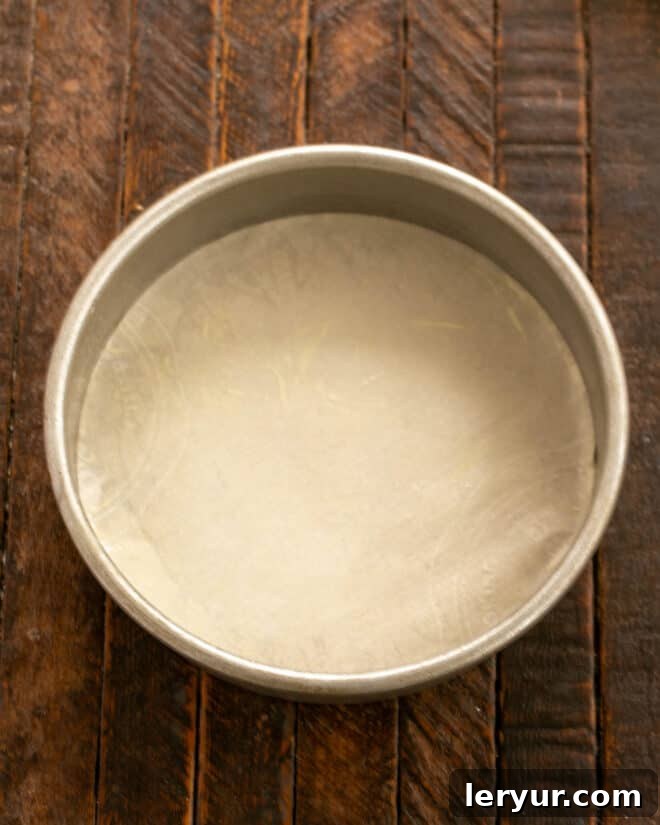 A round cake pan being prepared for baking, greased and floured or lined with parchment paper.