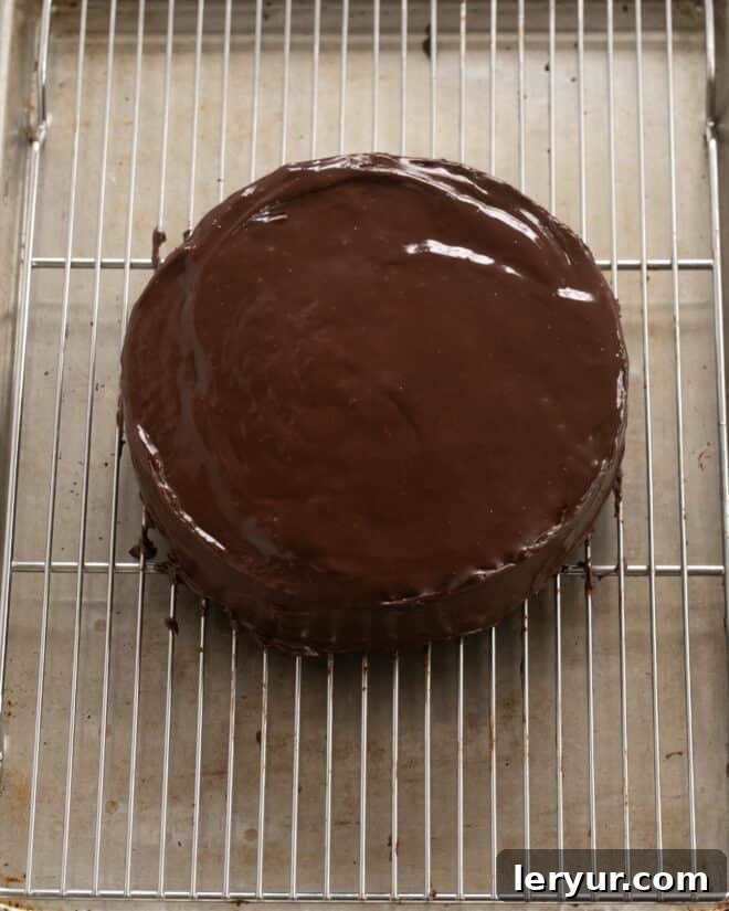 The cooled fudge cake being generously coated with the prepared chocolate ganache, creating a smooth, glossy finish.