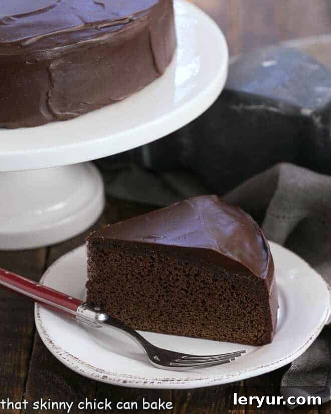 A perfectly sliced piece of One Layer Fudge Cake, showcasing its moist texture and rich ganache, resting on a white plate with a red-handled fork beside it.