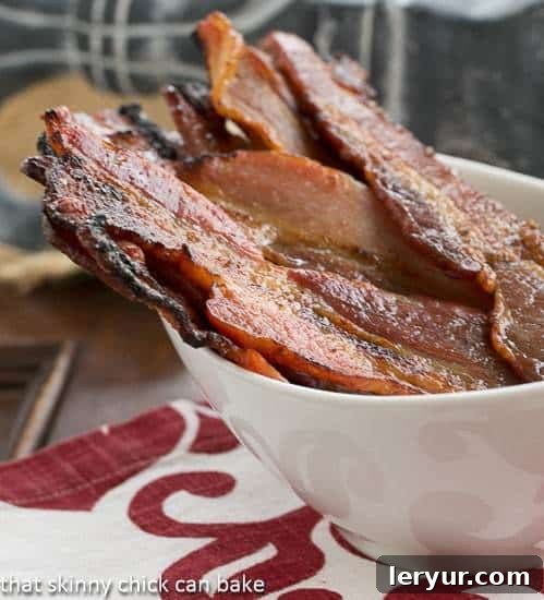 A bowl of glossy, caramelized Candied Bacon, also known as Pig Candy, viewed from the side. The bacon strips are perfectly glazed and ready to be enjoyed as a sweet and salty treat.