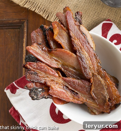 A close-up, overhead view of Candied Bacon, also called Pig Candy, served in a white bowl. The bacon strips are glistening with a sweet, caramelized glaze, ready for enjoyment.