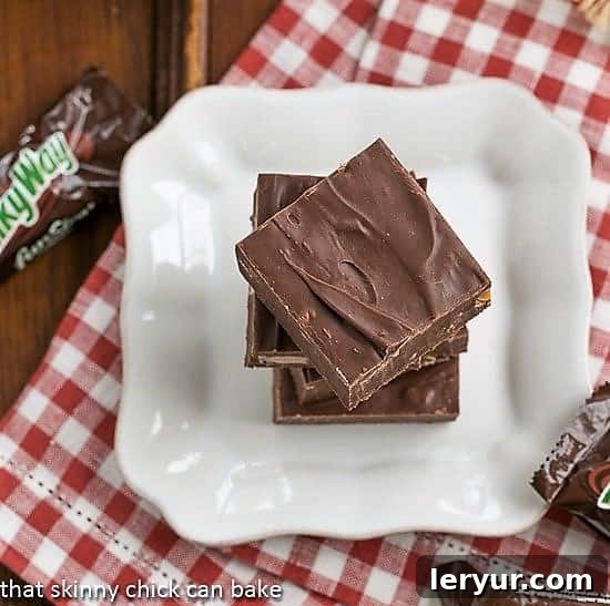 Milky Way Fudge squares stacked on a white plate over a red and white checked napkin.