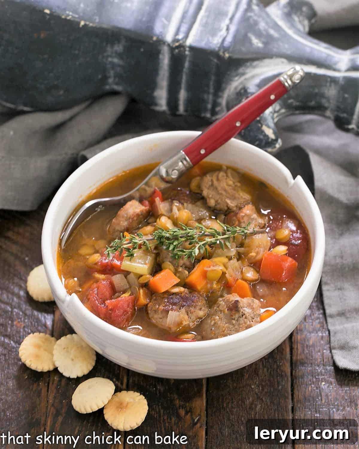 Sausage, Lentil and Vegetable Chowder: a hearty soup that will hit the spot on a chilly winter's night White bowl filled with hearty sausage lentil soup, garnished with fresh herbs and served with oyster crackers. A perfect cold weather meal.