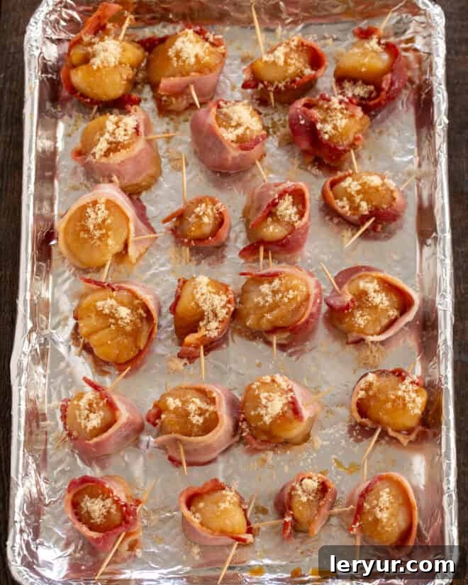 Maple Glazed Bacon Wrapped Scallops 6 A hand wrapping a raw scallop with a partially cooked strip of bacon.