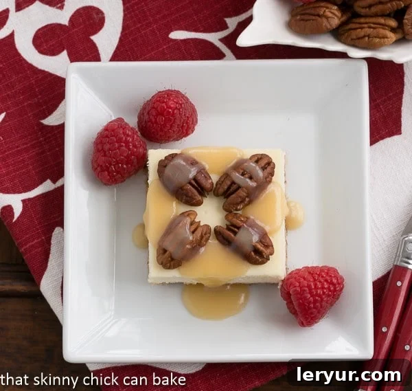 Golden Caramel Pecan Cheesecake Bars on a pristine square white plate, set against a charming red and white checkered napkin. The bars feature a visible nutty crust, a smooth cheesecake layer, and are generously topped with pecan halves and a glistening caramel drizzle.