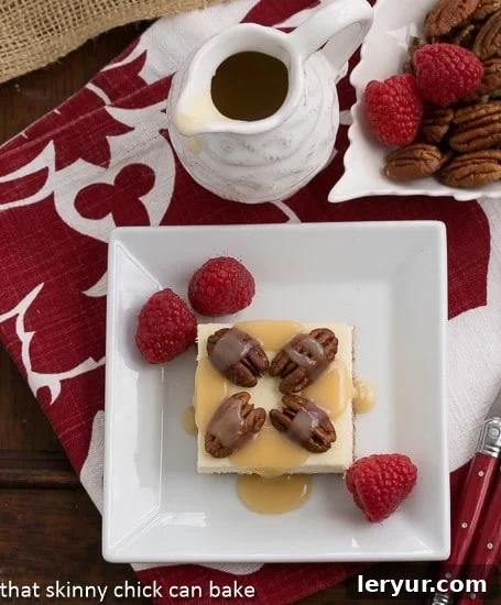 Overhead view of several Caramel Pecan Cheesecake Bars arranged on a square white plate, elegantly garnished with fresh raspberries alongside the pecan and caramel topping.