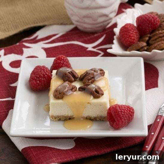 Caramel Pecan Cheesecake Bars drizzled with caramel and topped with pecans on a square, white ceramic plate, ready to be enjoyed.