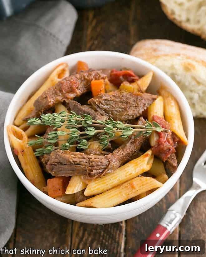 Beef Ragu with penne pasta in a white bowl with bread slice and a fork.