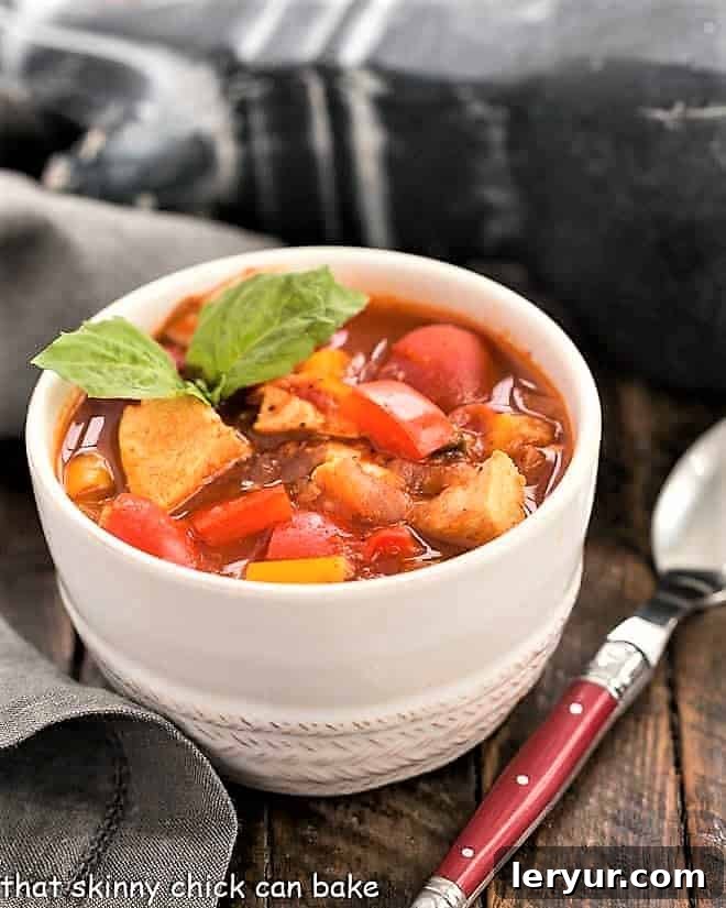 A close-up shot of Chicken and Bell Pepper Chili in a small white bowl, garnished with a fresh basil leaf.