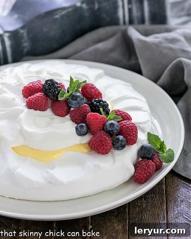 Lemon Pavlova on a white serving plate garnished with berries and mint, presented beautifully