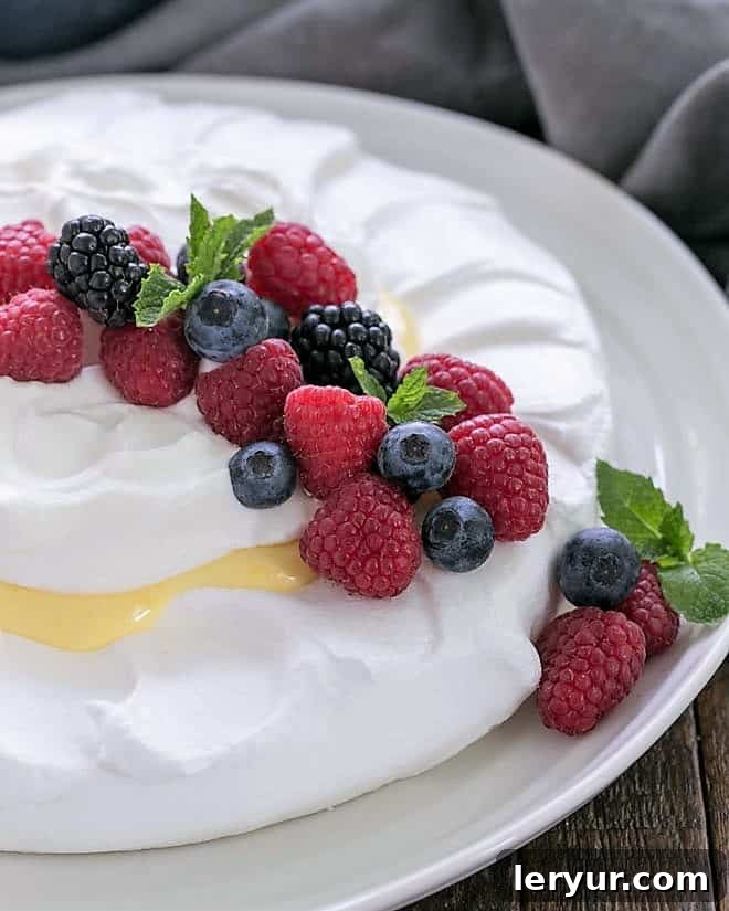 Lemon Pavlova on a white serving plate garnished with berries and mint, ready to be served