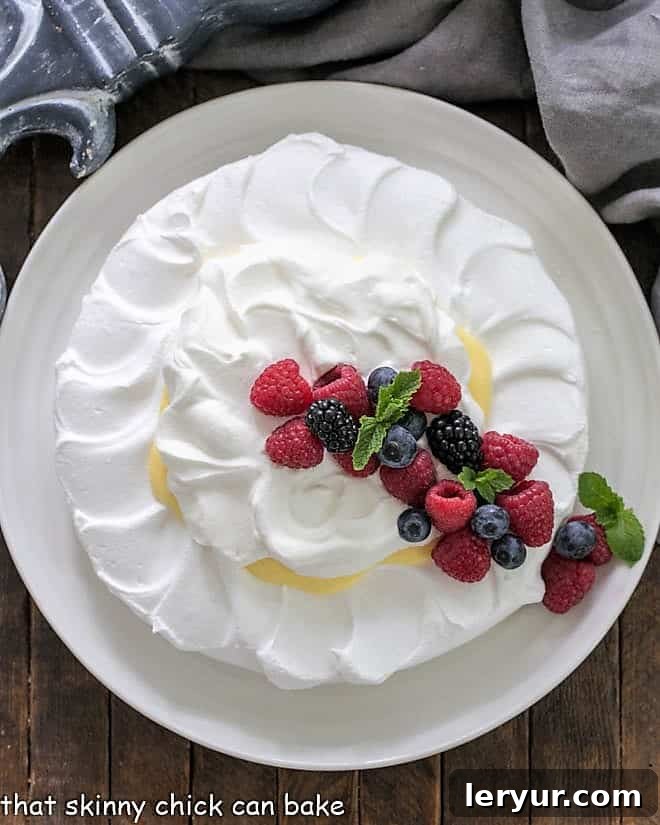 Overhead view of a pavlova dessert topped with lemon cream, whipped cream and fresh berries with mint garnish