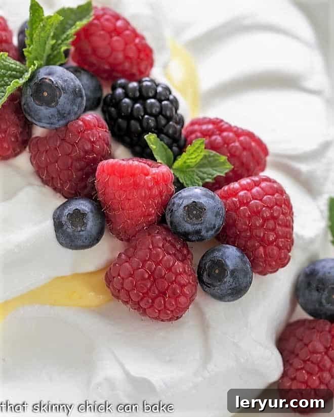 Vibrant fresh berries and mint artfully arranged on top of a crisp meringue shell, ready for lemon curd and cream