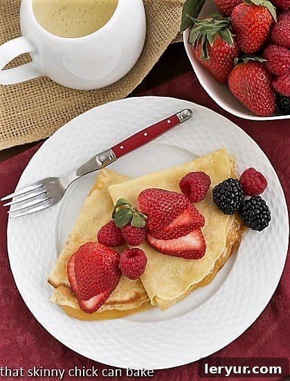 Butter and Rum Crêpes - Enhanced with Grand Marnier and rum, and filled with vibrant lemon curd, these are beyond ordinary crepes! An inviting overhead shot of delicious Butter and Rum Crêpes artfully arranged on a pristine white plate, accompanied by a fork with a striking red handle, highlighting their culinary appeal.
