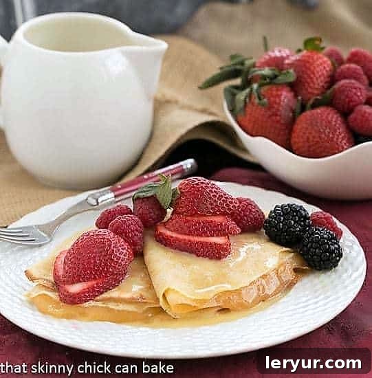 Golden Rum Crêpes with Bright Lemon Curd 2 Artfully presented Butter and Rum Crêpes on a clean white plate, adorned with a vibrant assortment of fresh berries, emphasizing their delicious appeal.