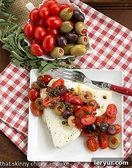 Mediterranean Baked Sea Bass with Tomatoes, Olives and Capers - An easy and healthy gourmet fish recipe. Perfectly baked Sea Bass with Tomatoes, Olives and Capers on a white plate, garnished with fresh herbs, viewed from above. It's a simple, gourmet Mediterranean dish.
