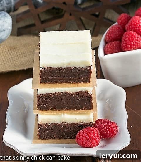 A close-up view of a perfectly baked Raspberry Brownie with White Chocolate Icing, sitting on a small white plate, with a bottle of Chambord liqueur subtly blurred in the background, hinting at the secret ingredient.