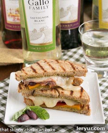 Sliced Mediterranean Grilled Cheese presented elegantly on a square white plate, garnished with fresh basil leaves and a few whole olives, highlighting its gourmet appeal