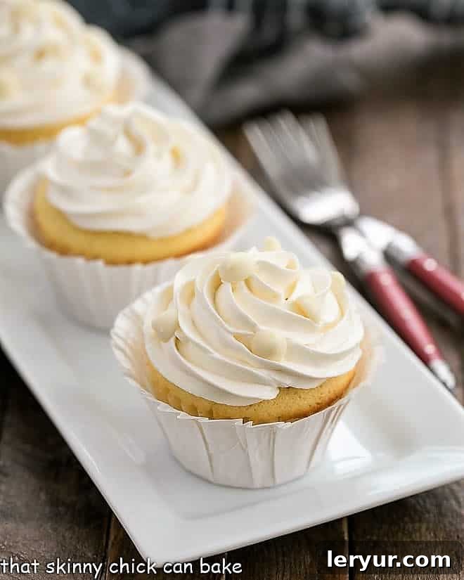 Ghirardelli Vanilla Cupcakes with White Chocolate Buttercream - tender vanilla cupcakes with a luscious swirl of Swiss meringue buttercream flavored with white chocolate! Ghirardelli Vanilla Cupcakes with White Chocolate Buttercream on a white ceramic tray.
