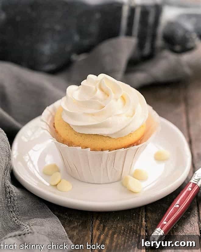 Ghirardelli Vanilla Cupcakes with White Chocolate Buttercream - tender vanilla cupcakes with a luscious swirl of Swiss meringue buttercream flavored with white chocolate! Ghirardelli Vanilla Cupcakes with White Chocolate Buttercream on a round white plate with white chocolate chips.