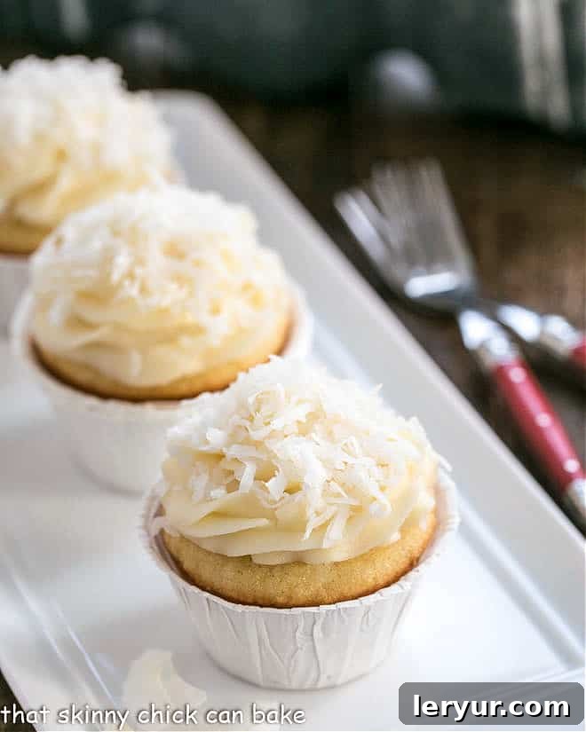 Freshly baked coconut cupcakes with cream cheese frosting on a white tray, garnished with shredded coconut.