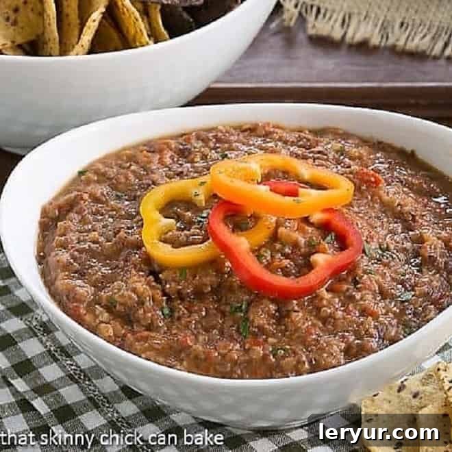 Smoky Black Bean Dip in a white bowl topped with fresh bell pepper rings, ready to be served with crunchy chips.