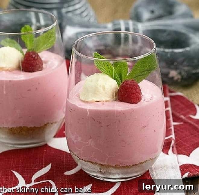 Raspberry Mousse in elegant parfait glasses, garnished with fluffy whipped cream, fresh raspberries, and a delicate mint leaf, presented on a rustic wooden surface.