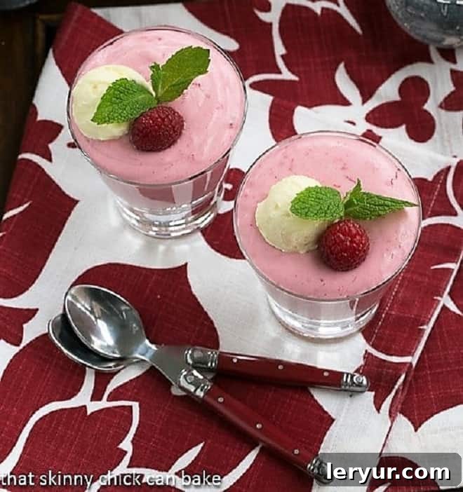 Raspberry Mousse elegantly presented in highball glasses, viewed from an aerial perspective. Each glass features a red-handled spoon resting on a charming red and white patterned napkin, suggesting a delightful tasting experience.