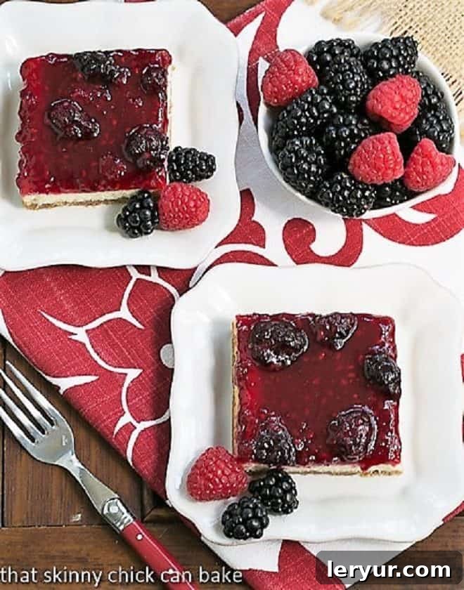 Berry Topped Cheesecake Bars served on square white plates next to a bowl of berries