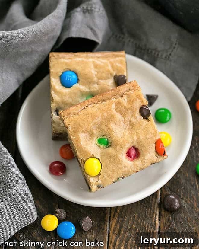 Overhead view of two M & M Blondies on a round white plate, showcasing their vibrant M&M candies and golden-brown crust.